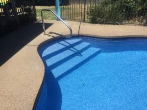 Swimming pool with blue water and metal ladder on concrete deck, metal railing visible in background