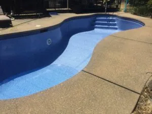 Empty swimming pool with blue tile interior and light blue pool deck, concrete surrounding deck with metal fencing and gates