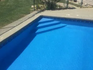 Swimming pool with bright blue water and steps, surrounded by concrete deck and green lawn with fencing