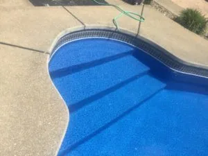 Overhead view of pool with blue interior and built-in steps, surrounded by concrete deck and green hose