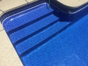 Swimming pool steps and floor with blue textured finish and dark shadow lines, concrete deck visible at top edge