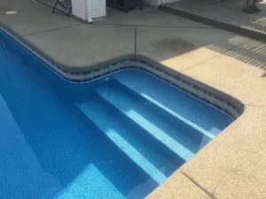 Swimming pool steps descending into blue water with concrete deck and pool equipment visible