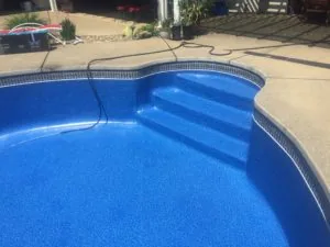 Empty blue swimming pool with concrete deck, curved edges, and white tile trim in sunny residential setting