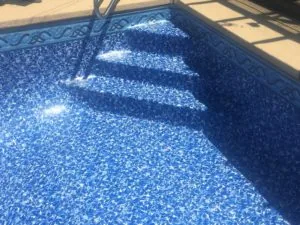 Blue tiled swimming pool with decorative border and sunlight reflecting off water surface