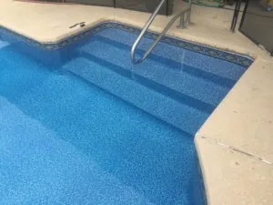 Swimming pool with blue tile interior and concrete deck with metal handrail and steps