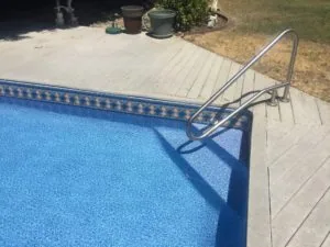 Metal pool ladder on deck next to blue swimming pool with decorative border tile