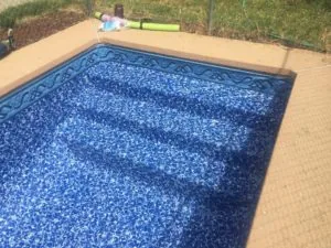 In-ground swimming pool with blue textured liner and decorative border, viewed from above with concrete deck surrounding it