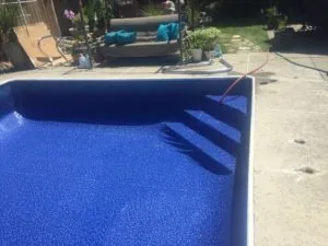 Swimming pool with blue interior wall and concrete deck, lounge chairs and landscaping visible in background