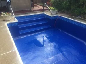 Empty swimming pool with blue interior, white coping, decorative tile border, and built-in steps