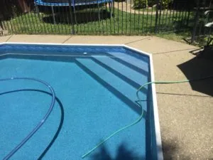 Swimming pool with blue water and coiled hoses on concrete deck, surrounded by black metal safety fence