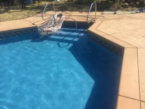 Swimming pool with blue water, concrete deck, and metal lounge chairs on sunny day