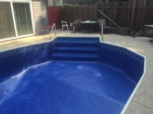 Empty in-ground swimming pool with blue interior and built-in steps in residential backyard