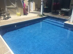 Blue swimming pool with patio deck, white building structures, and lounge chairs in background