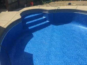 Empty residential swimming pool with blue interior and built-in steps, surrounded by concrete deck and yard