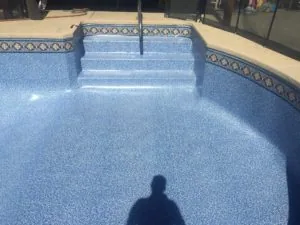 Empty residential swimming pool with blue textured interior, decorative tile border, and concrete deck