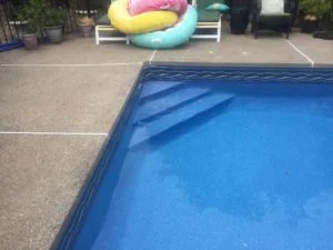 Swimming pool with blue water and decorative steps, surrounded by concrete deck and colorful inflatable floats on lounge chairs