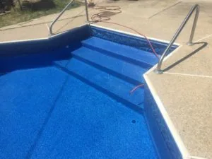 Empty swimming pool with blue interior, steps, metal handrails, and red hoses on concrete deck
