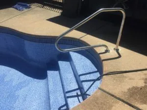 Metal handrail attached to pool stairs with blue tiled steps visible in water