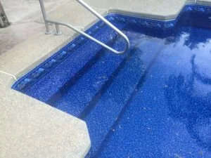 Swimming pool steps with metal handrail leading into blue water with textured surface