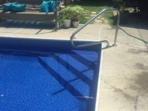 Metal handrail beside swimming pool with blue water and concrete deck