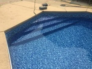 In-ground swimming pool with blue tile interior and decorative border, viewed from above on concrete deck with equipment and hoses nearby