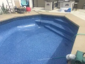 Empty residential swimming pool with blue textured interior and concrete deck surrounded by patio furniture and equipment