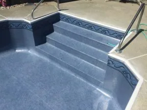Empty swimming pool with blue interior, decorative tile border, and built-in steps leading into shallow end