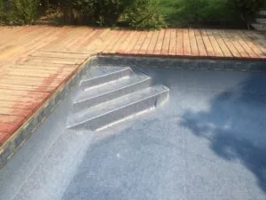 Covered swimming pool with three rectangular skylights next to wooden deck surrounded by trees