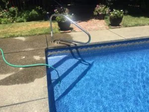 Swimming pool with metal ladder and green hose, surrounded by brick patio, grass, and flowering planters