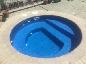 Empty in-ground swimming pool with blue plaster interior and concrete deck surround