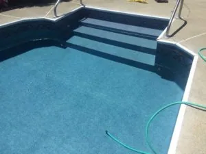 Empty residential swimming pool with blue interior and steps, surrounded by concrete deck and metal railings
