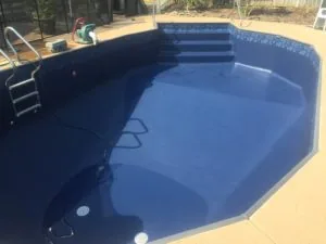 Empty in-ground swimming pool with blue interior liner, metal ladder on left side, and concrete deck surrounding the basin