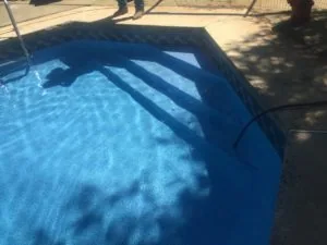 Empty swimming pool with blue interior and ladder, viewed from above with concrete deck and shadows visible
