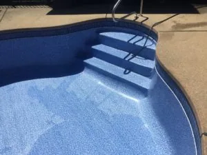 Swimming pool with blue tile interior, light blue plaster floor, and entry steps with metal handrails