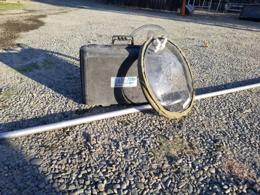 Metal suitcase and circular metal strainer with hose on gravel ground