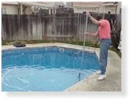 Person in pink shirt using pole tool to clean empty swimming pool