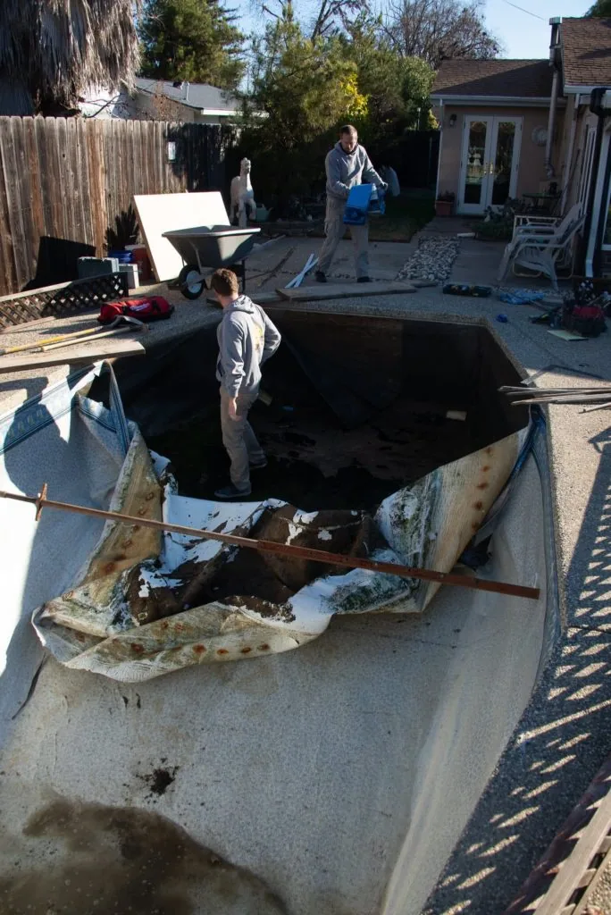 Large metal pool shell undergoing renovation in a residential backyard with workers and equipment