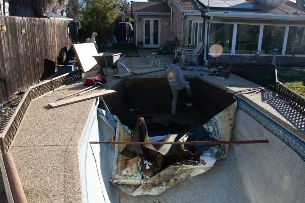 Large landscaping debris and construction waste in truck bed at residential property with houses and yard visible in background
