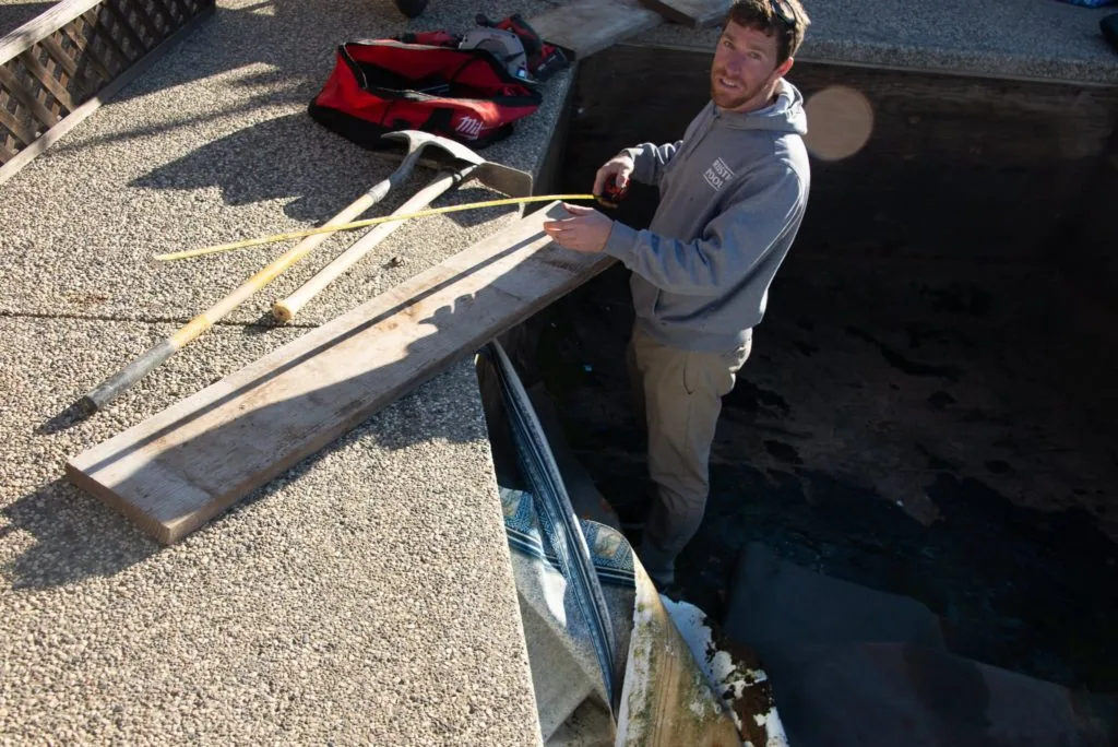 Man holding pool cleaning equipment on concrete pool deck next to in-ground pool