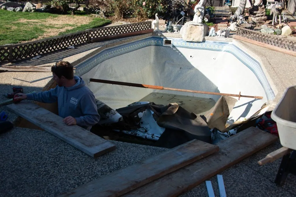 Worker cleaning empty residential swimming pool with brush and skimmer net