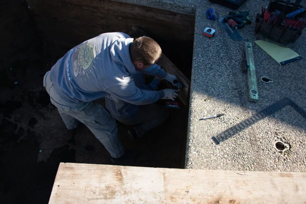 Worker in blue shirt leaning into dark underground opening or tank during construction or maintenance work