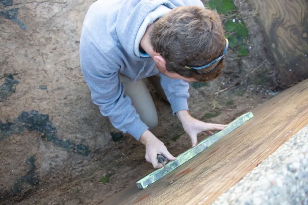 Person in blue shirt using measuring tool on wooden board during outdoor construction work