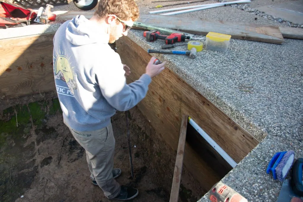 Person working on wooden structure with construction materials and tools scattered nearby on gravel surface