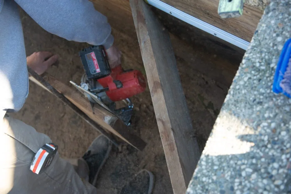 Person holding red and black power tool over wooden framing during construction work