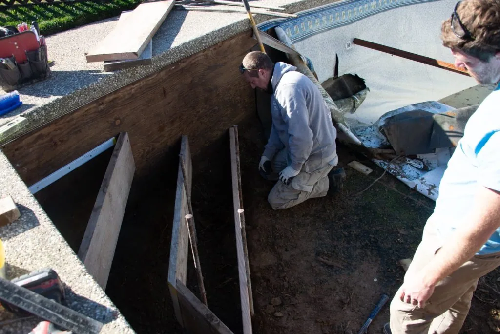 Two workers installing wooden frame sections into a swimming pool under construction