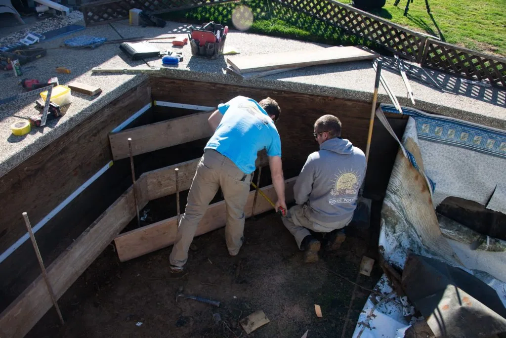 Two workers excavating an in-ground pool foundation with wooden framing in a residential backyard