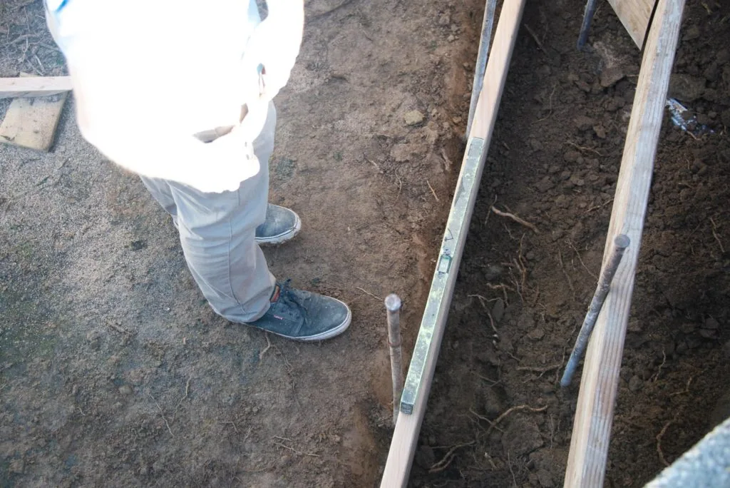 Person wearing boots standing next to wooden garden bed frames on bare soil