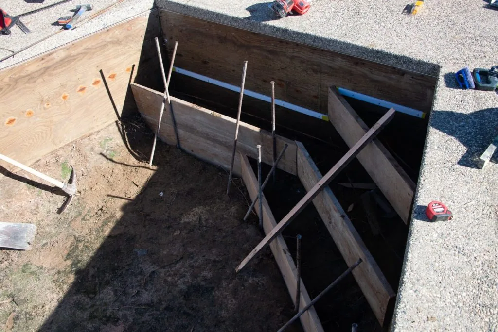Overhead view of wooden pool structure under construction with metal rebar supports and blue piping visible inside dark wooden framing