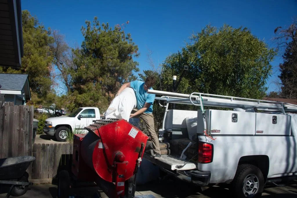 Worker loading red equipment onto white work truck bed with roof rack