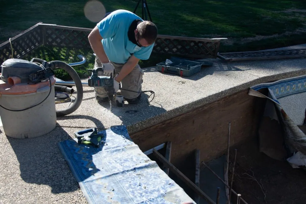 Man in blue shirt working on pool maintenance with pump equipment and containers on concrete deck